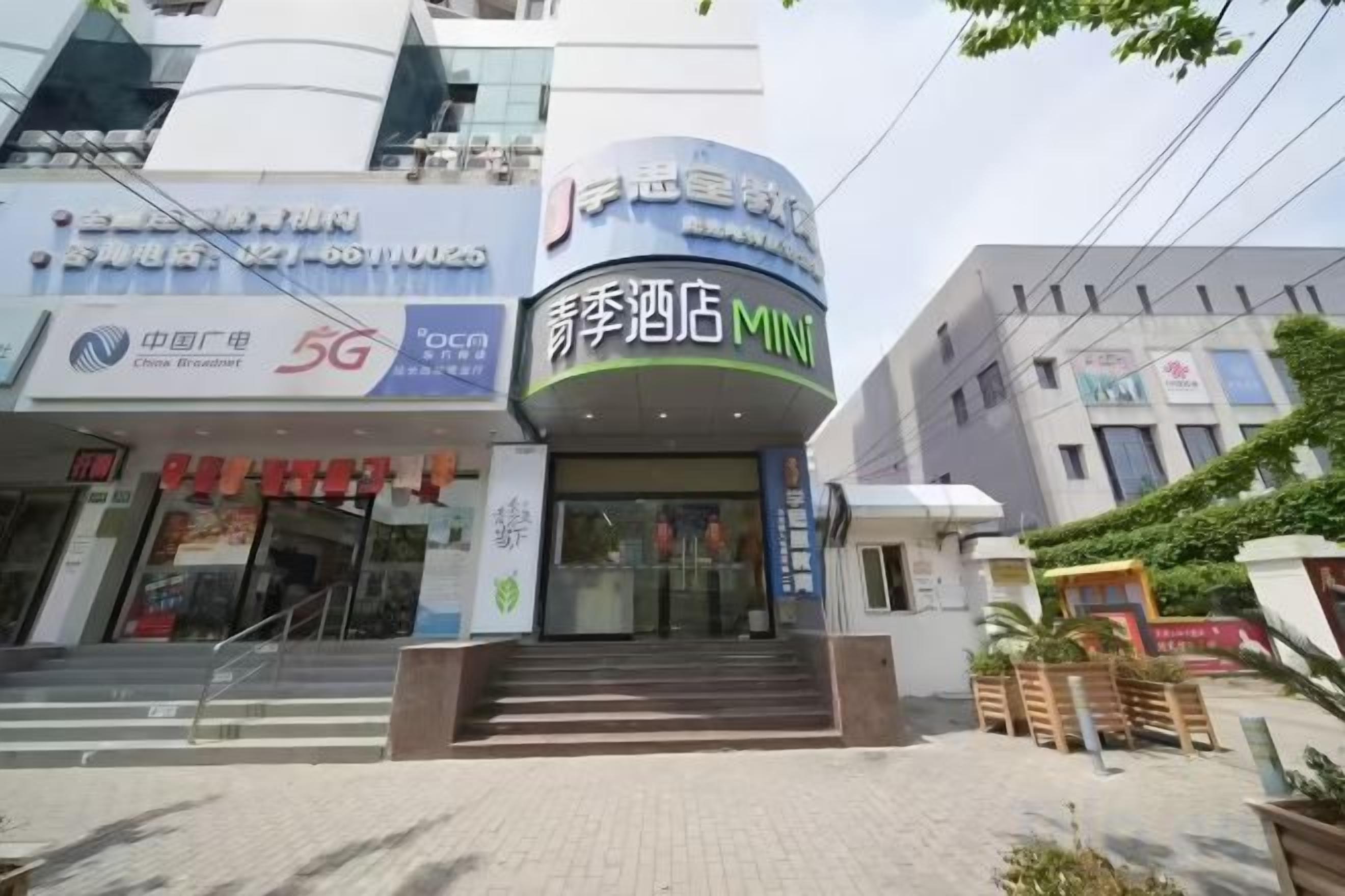 Entrada de un hotel con un letrero que dice 'Shenzhen Hotel Mini' y un anuncio de servicio 5G.