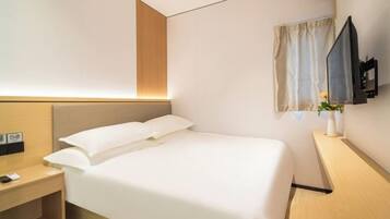 A hotel room with a bed, bedside table, TV, and a small desk area.