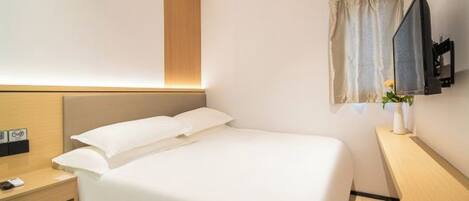 A hotel room with a bed, bedside table, TV, and a small desk area.