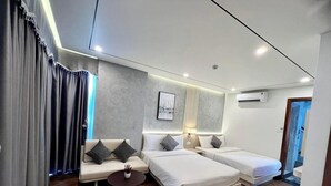Una habitación de hotel moderna con un sofá, dos camas, una mesita redonda y un ventanal con cortinas.