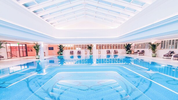 A large indoor swimming pool with clear blue water, surrounded by lounge chairs and potted plants. - Renhe Spring Hotel (Chengdu)
