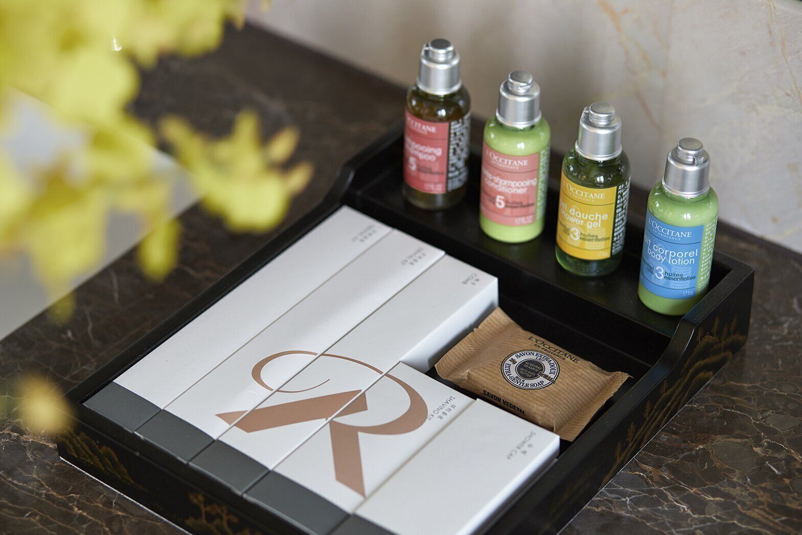 A set of L'OCCITANE body care products in a black tray on a marble countertop.
