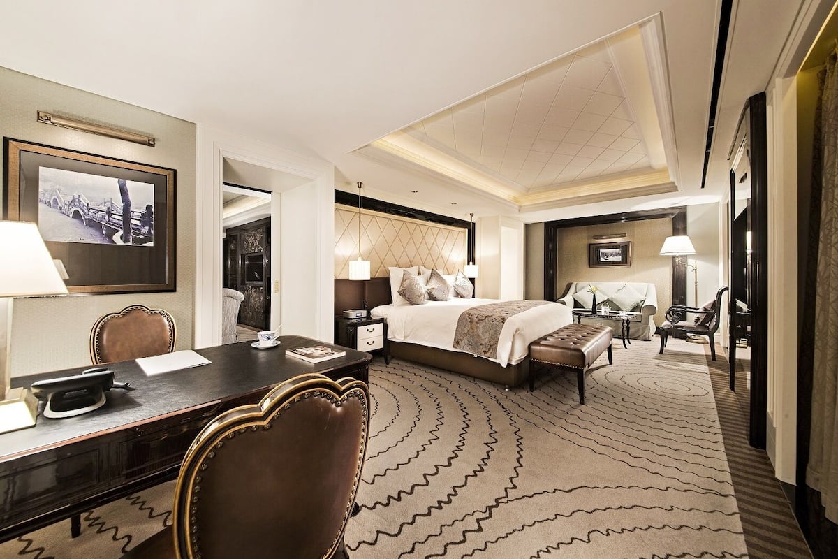 Quarto de hotel com uma cama grande, uma escrivaninha, uma cadeira, um abajur e um quadro na parede.