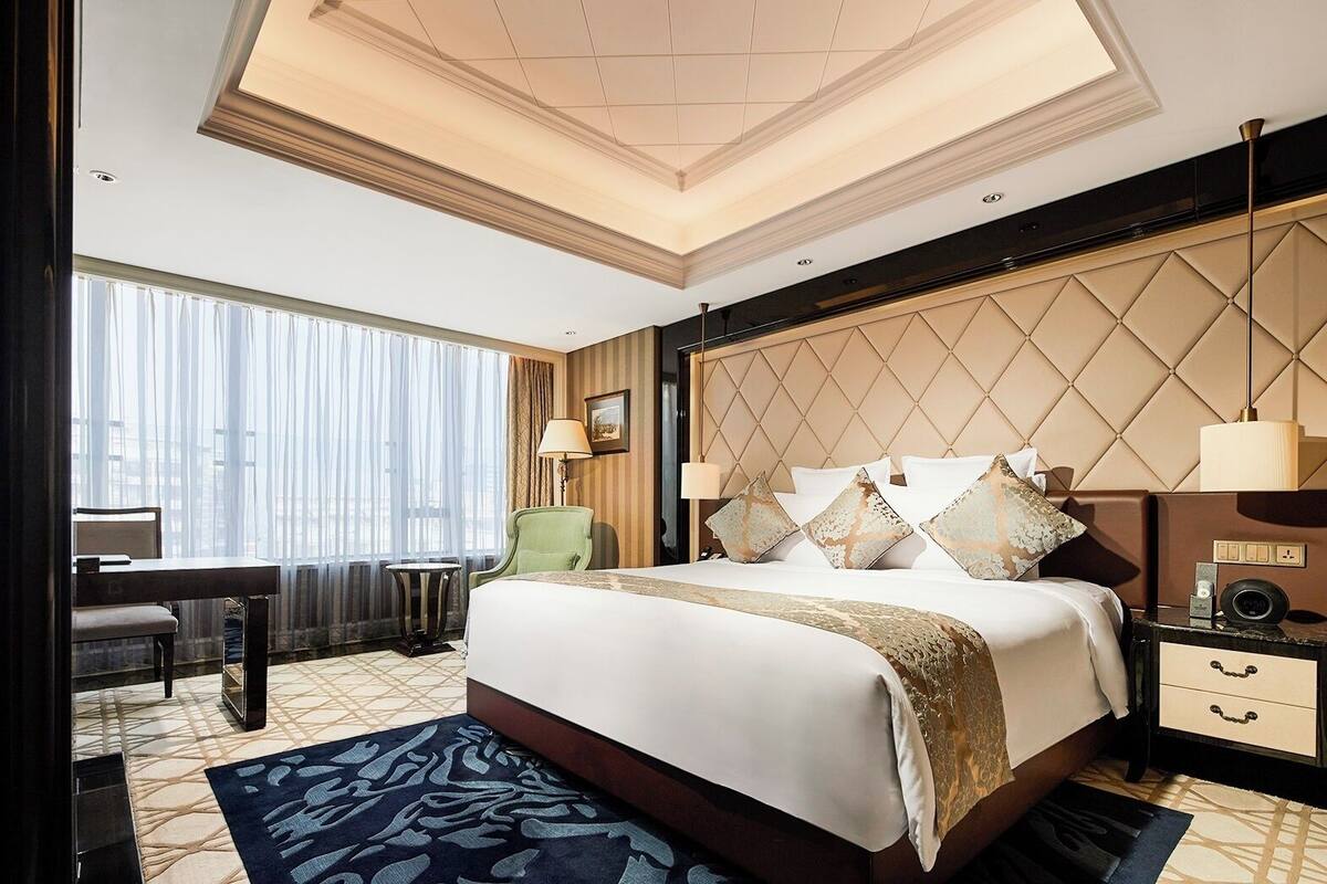 Quarto de hotel com uma cama grande, uma escrivaninha, uma cadeira e uma mesa de cabeceira com abajur.