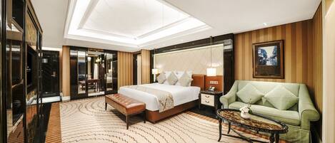 A hotel room with a large bed, a green armchair, a small table, and a mirror.