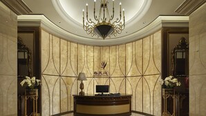 A reception area with a marble wall, a chandelier, a reception desk, and two ornate side tables with vases. - Renhe Spring Hotel (Chengdu)