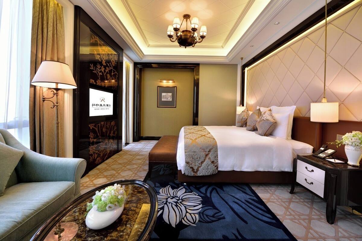 Quarto de hotel com cama, mesa de cabeceira, luminária e um vaso decorativo.