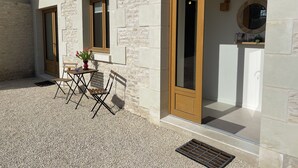 A stone building with a small patio area featuring a table and chairs, a potted plant, and a door leading to a room.