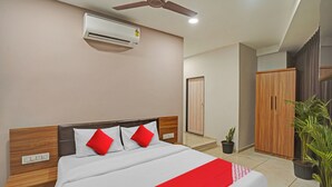 A hotel room with a bed, a ceiling fan, an air conditioner, a wardrobe, and potted plants. - Hotel Santeria Inn (Surat)