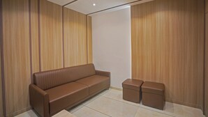A modern room with a brown leather sofa, a matching ottoman, and wooden panel walls. - Hotel Santeria Inn (Surat)