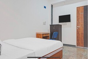 A bedroom with a bed, a desk, a chair, a wardrobe, and a TV mounted on the wall.