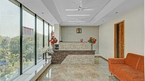 A reception area with a marble counter, a wooden door, and a red sofa. - Hotel Santeria Inn (Surat)