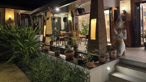 Un espacio exterior con plantas en macetas, una estatua y una zona de estar con sillas y una mesa.