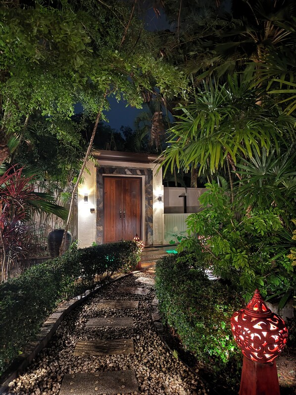 Un camino que lleva a una puerta de madera, con un muro de piedra y un farolillo rojo decorativo.