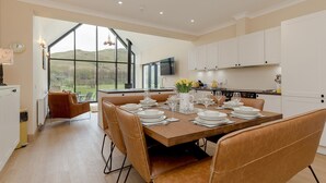 A modern kitchen with white cabinets, a dining table set with plates and glasses, and a large window offering a view of the outdoors. - Balbeg Cottage by Interhome (Ayr)