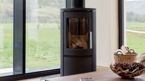 A modern living room with a black wood-burning stove, large windows, and a view of the outdoors. - Balbeg Cottage by Interhome (Ayr)