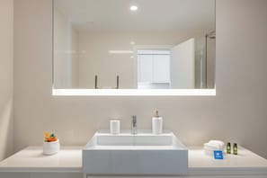 Une salle de bain moderne avec un grand miroir, un lavabo blanc et une petite plante en pot.