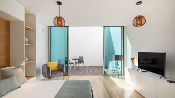 Habitación de hotel moderna con cama, televisión, zona de estar con mesa y sillas, y balcón con vistas.