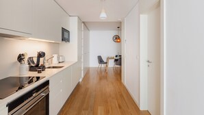 Un pasillo estrecho con una zona de cocina a un lado, que incluye una estufa, un fregadero y armarios. Se observa un comedor con mesa y sillas a lo lejos.
