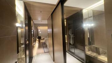 A modern hotel corridor with mirrored walls, a clean floor, and a well-lit hallway leading to a room with a bed and a desk.