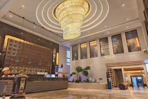 A hotel lobby with a reception desk, a large chandelier, and a reception area with a decorative wall. - Shanghai Grand Hotel (Shanghai)