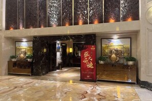 Un hall d’hôtel avec un sol en marbre, un comptoir d’accueil et une grande enseigne rouge.