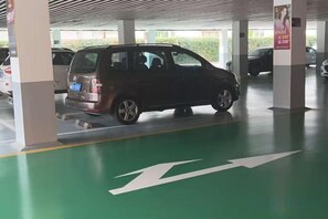 A parking garage with a green directional arrow on the floor, a parked car, and pillars supporting the structure. - Shanghai Grand Hotel (Shanghai)