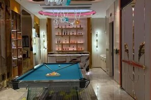 Une table de billard dans une chambre d’hôtel, avec un mini-bar et une étagère remplie de bouteilles.