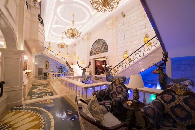 A grand lobby with a staircase, ornate chandeliers, and a large animal statue.