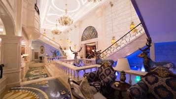 A grand lobby with a staircase, ornate chandeliers, and a large animal statue.