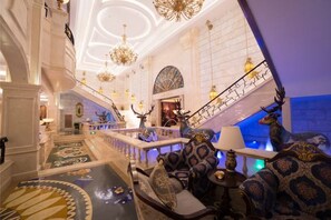 A grand lobby with a staircase, ornate chandeliers, and a large animal statue.