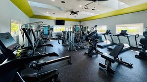 Et fitnesscenter med forskellig træningsudstyr, herunder løbebånd og styrkemaskiner, samt en ventilator i loftet.