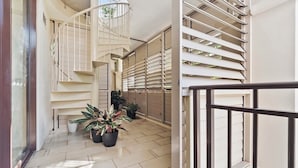 Un interior moderno con una escalera de caracol, plantas en macetas y un balcón con contraventanas blancas.