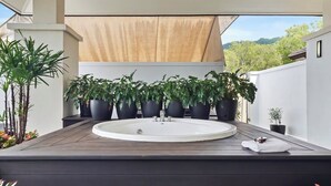 Un baño al aire libre moderno con un lavamanos grande, varias macetas con plantas y una terraza de madera.