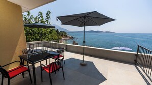 Une terrasse avec une table et des chaises, un parasol et une vue sur la mer.