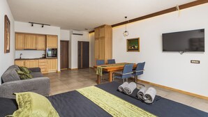 Un salon moderne avec un canapé, une table à manger et des chaises, un téléviseur fixé au mur, et une cuisine en arrière-plan.