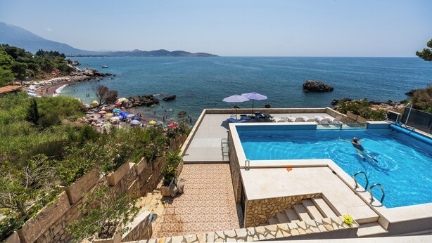 Une piscine avec vue sur la mer, une plage avec des parasols et un paysage rocheux.