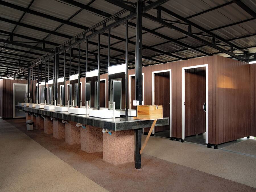 A row of bathroom stalls with sinks and mirrors, a trash bin, and a wooden box on a counter.
