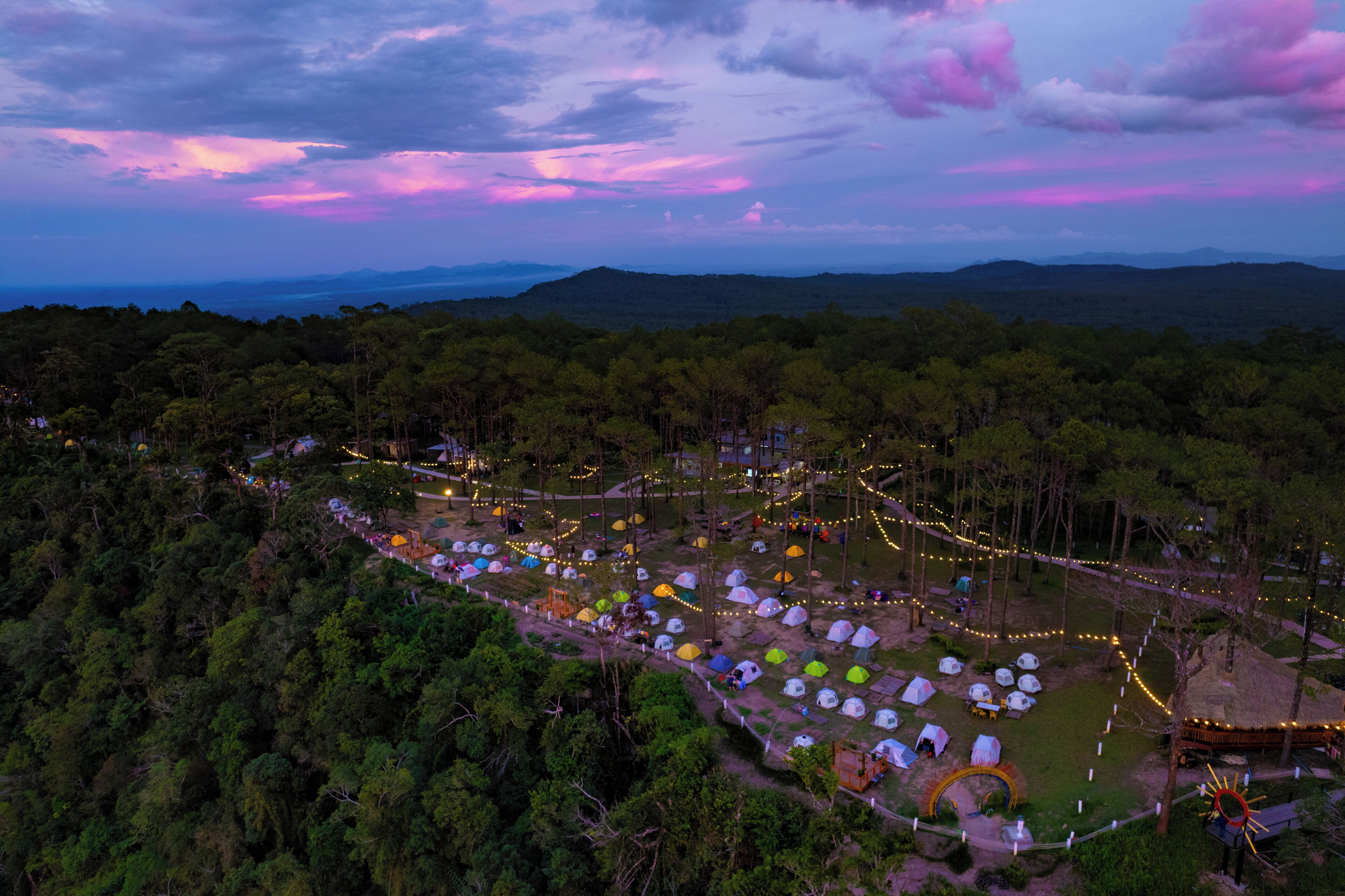 Un terrain de camping avec des tentes et des arbres, entouré de montagnes.