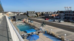 A pool area with umbrellas, a Coca-Cola refrigerator, and a view of the street and houses. - Oceanview Condo in Wildwood Crest – Steps from the Beach! (Wildwood Crest)