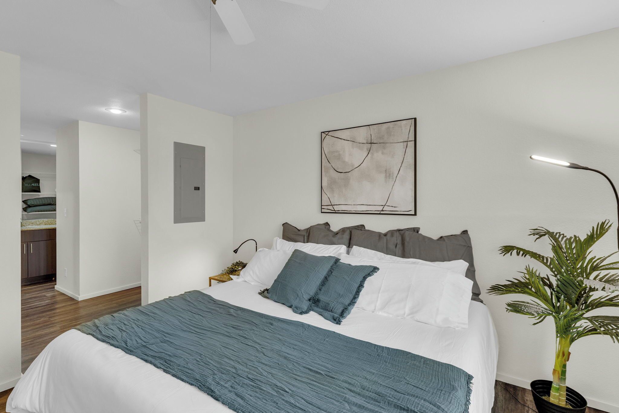 Ein Schlafzimmer mit Bett, Nachttisch, Lampe, Wandbild und einer Topfpflanze.