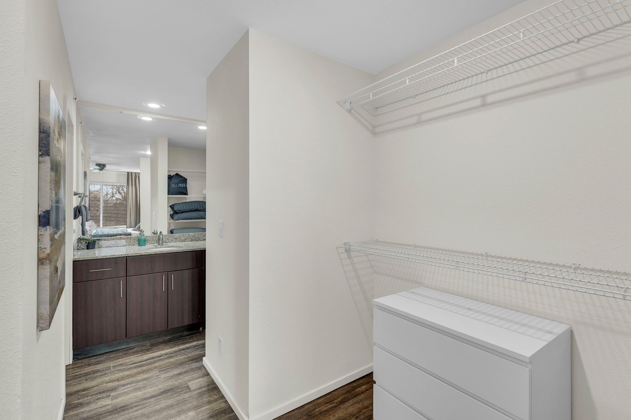 A narrow hallway with a kitchen area on the left, featuring dark wooden cabinets and a white countertop. A white radiator is mounted on the right wall.