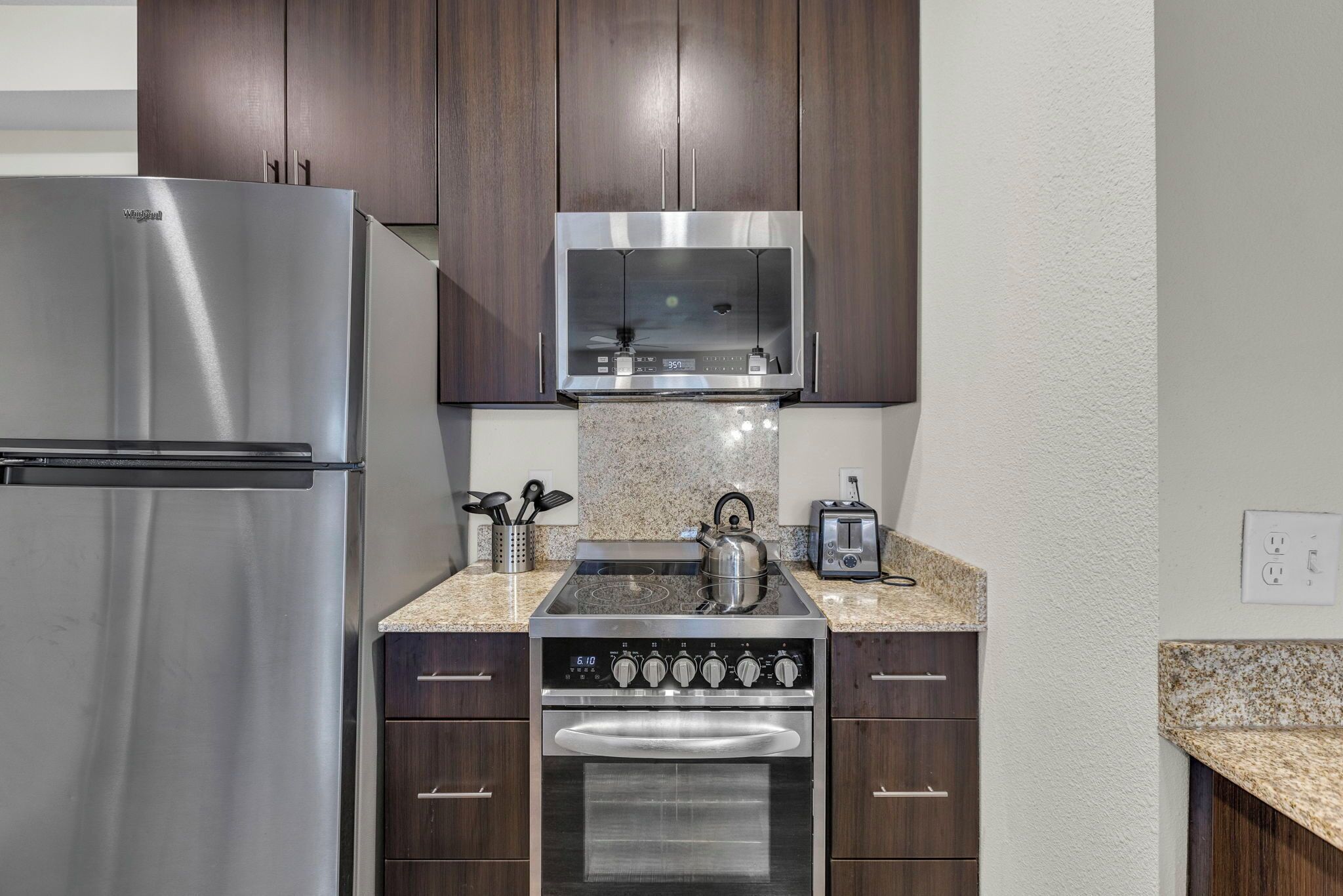 A modern kitchen with stainless steel appliances, dark wooden cabinets, granite countertops, and a built-in oven.