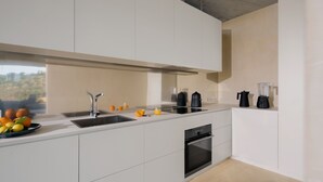 A modern kitchen with white cabinetry, a built-in oven, and a window with a view of greenery. - Villa Esovisia by Elite Villas (Avola)