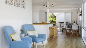 Una sala moderna con dos sillones azules, una mesa de centro de madera y un comedor con mantel estampado en zigzag.