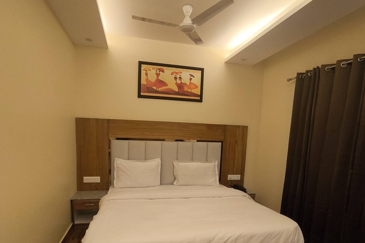 A bedroom with a bed, a ceiling fan, a nightstand, a chair, and a picture on the wall.
