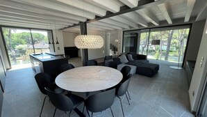 Une cuisine moderne avec une table de salle à manger ronde et des chaises noires, un grand lustre et une vue sur l’extérieur.