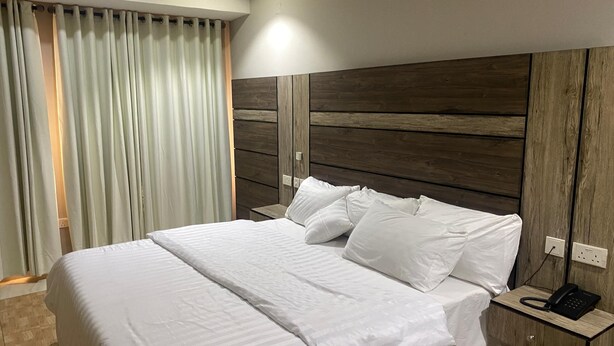 Un letto rifatto con lenzuola bianche, una testiera in legno e un comodino con un telefono.