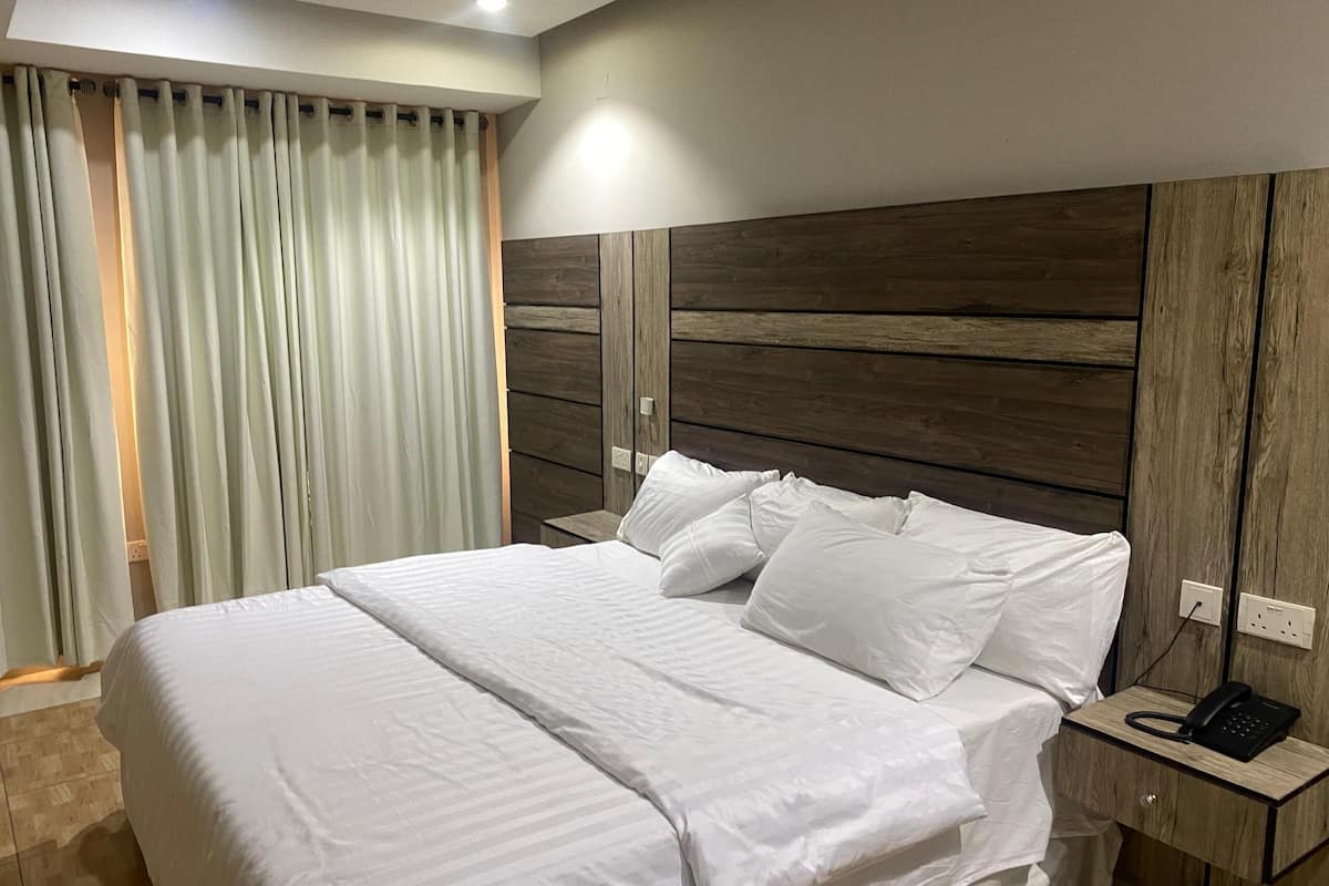 Un lit bien fait, avec du linge de lit blanc, une tête de lit en bois et une table de chevet sur laquelle se trouve un téléphone.