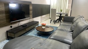 Un soggiorno moderno con un'ampia televisione a schermo piatto, un mobile porta TV in legno scuro, un tavolino rotondo con un vaso di fiori e un divano in pelle grigia.
